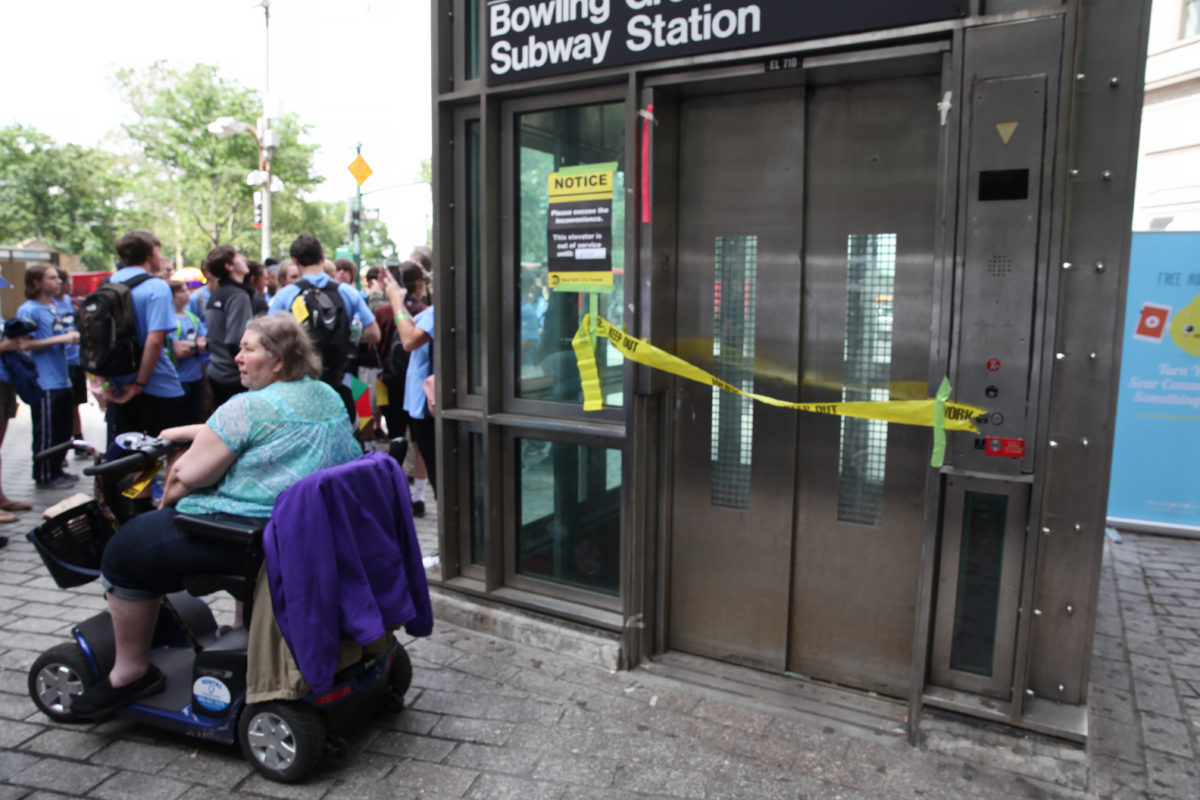 Person in electric wheelchair outside a closed subway station elevator blocked off with tape by the Bowling Green Stop in New York