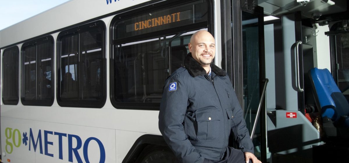 Smiling Bus Operator in uniform facing hte camera infront of Cincinnati bus