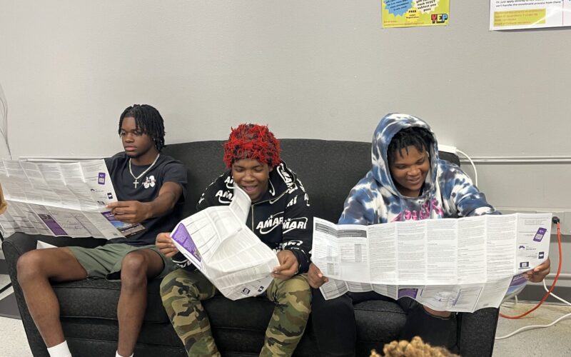 Three young adults read the RTA New Orleans transit schedule.