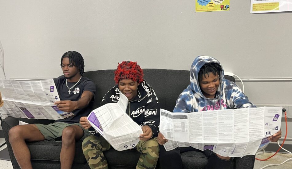Three young adults read the RTA New Orleans transit schedule.